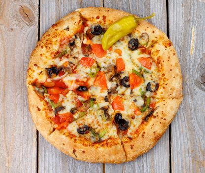 Hot Vegetarian Pizza with Tomatoes, Black Olives and Jalapeno Pepper on Rustic Wooden background. Top View