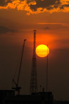 Industrial construction cranes and building silhouettes over sun at sunset.