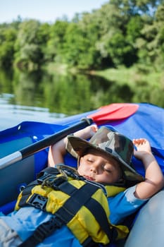 Cute little boy sleeping in kayak on the river at a lovely summer day.