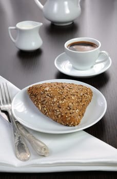 Bun with cereals with a cup of coffee and milk on the table