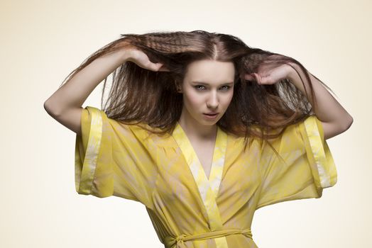 sexy woman with long brown hair wearing yellow transparent nightgown looking in camera and having hands in the hair