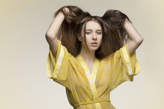 sensual female wearing sexy yellow nightgown posing with hands in the long brown hair