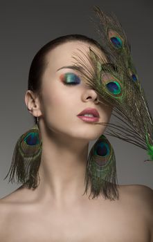 portrait of pretty brunette girl with make-up and accessory inspired by peacock feathers