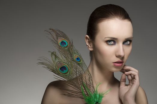 close-up beauty portrait of sexy female with brown hair-style posing with elegant make-up and accessory inspired by peacock���s feather