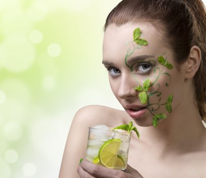 close-up portrait of pretty girl with green creative make-up and some mint leaves on the face, drinking mojito