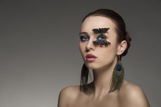 close-up portrait of sexy woman with brown hair and make-up and accessory inspired by peacock feathers