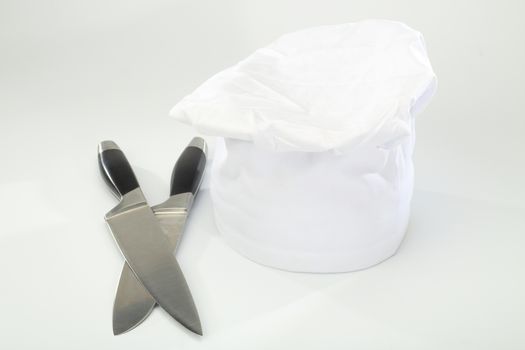  chef's hat and cooking knifes over white
