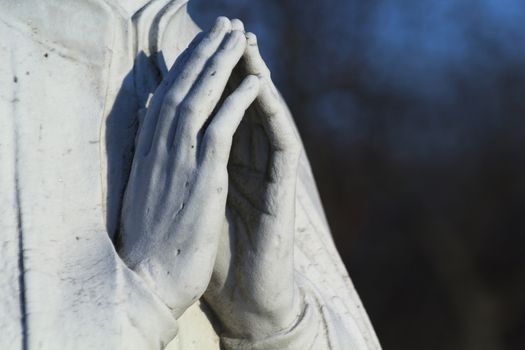 Stone statue of praying hands lit by the setting sun. 