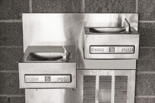 Wall mounted pair of shining metal drinking fountains. One for adult and one for children or the handicapped.