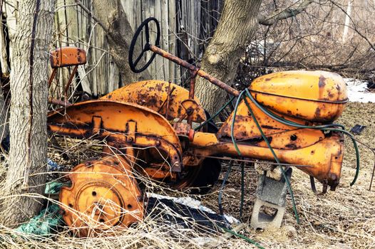 Vintage and abandoned yellow rusting tractor. It is missing wheels and paint.