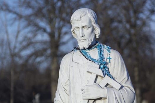 Stone statue of Catholic Saint with blue rosary beads. 