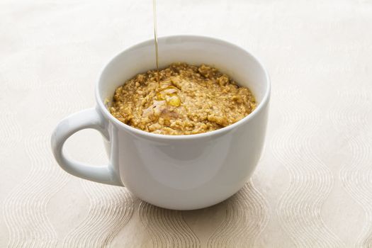 cup filled with oatmal with maple syrup being poured on top