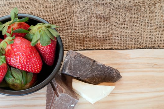 Strawberries in a blck bowl and Chocolate on a wooden board