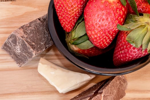 Strawberries and Chocolate in a bowl on the right on a wooden board 