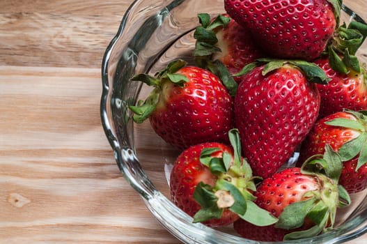 Strawberries in a glass bowl on a wooden board