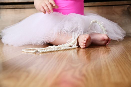 Baby ballerina feet on a wooden floor in white tutu