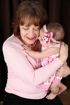 Grandmother and granddaughter cuddling against brown background