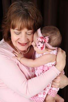 Grandmother and granddaughter cuddling against brown background