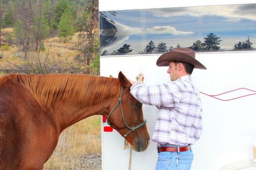 Young cowboy grooming his horse at the trailor 