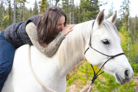 Beautiful brunette female spending time with her white horse