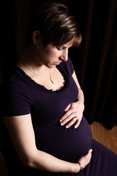 Pregnant woman against dark background with uneven lighting