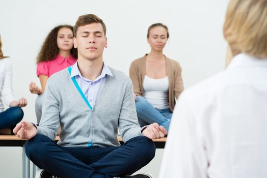 group of young people meditating in office at desk, group meditation