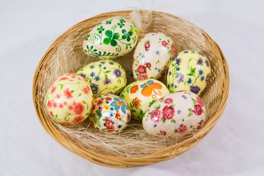 Group of colorful easter eggs decorated with flowers made by decoupage technique, in a basket on light background
