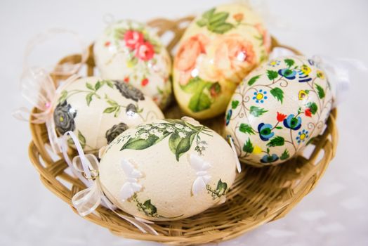 Group of colorful easter eggs decorated with flowers made by decoupage technique, in a basket on light background