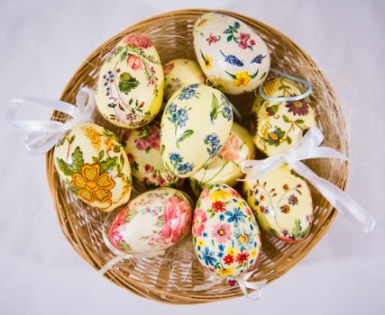 Group of colorful easter eggs decorated with flowers made by decoupage technique, in a basket on light background