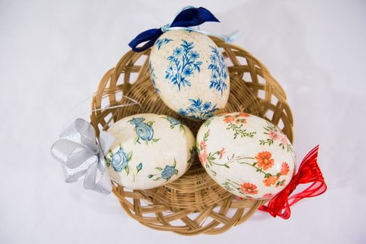 Group of colorful easter eggs decorated with flowers made by decoupage technique, in a basket on light background