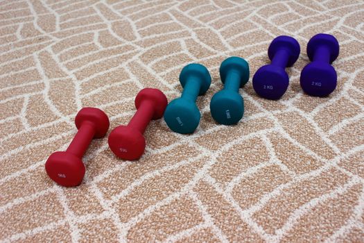 On the brown carpet on three pairs of dumbbells of different weights and different colors for sports
