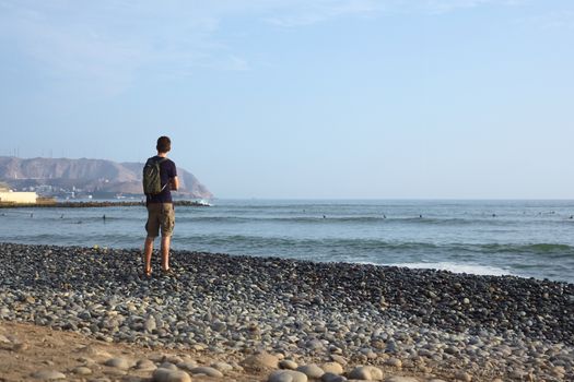 LIMA, PERU - APRIL 2, 2012: Unidentified young man standing on the rocky Pacific coast of Miraflores watching in the direction of the district of Chorrillos on April 2, 2012 in Lima, Peru. 