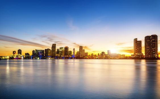 Miami city skyline panorama at dusk with urban skyscrapers over sea with reflection 