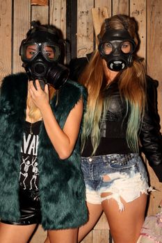 Two women in front of a wooden wall with gasmasks.