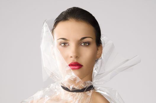 beauty portrait of young brunette with red lips and cellophane around her face, she is in front of the camera and looks in to the lens