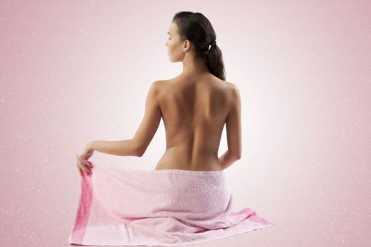 naked brunette showing her back shoulder and covering her body with a pink towel
