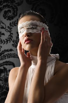 pretty young woman with dark hair wearing a white shirt and a white lace mask on black background