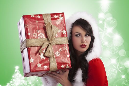 Sexy model in a red christmas dress with short skirt and hood with white fur and a big gift box over light green and christmas trees