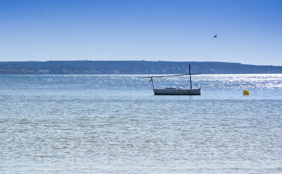 Traditional Majorcan boat - llaut. Traditional llaut moored by a yellow buoy, glittering ocean, seagull and blue sky. Summertime, Majorca, Balearic islands, Spain.