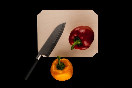 two peppers with knife on wooden cutting board on black background
