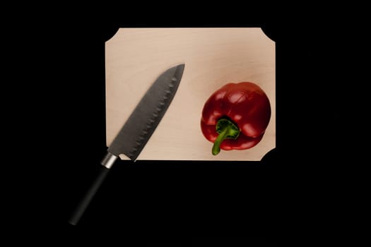 pepper with knife on wooden cutting board on black background