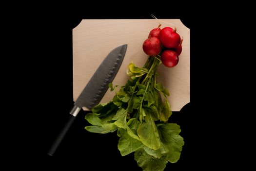 radish with knife on wooden cutting board on black background