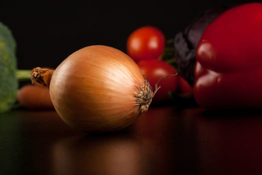 onion on black with different vegetables in the background