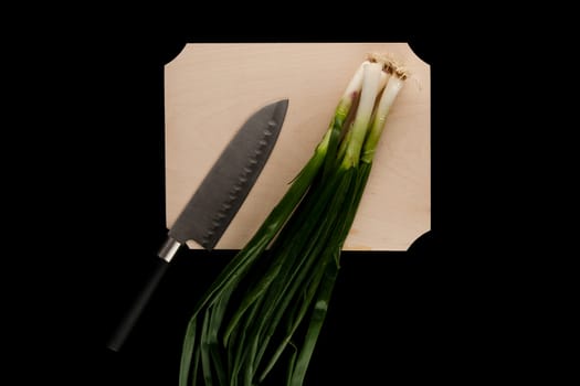 green onions with knife on wooden cutting board on black background