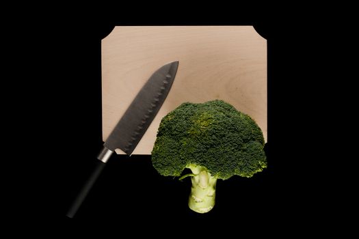 broccoli with knife on wooden cutting board on black background