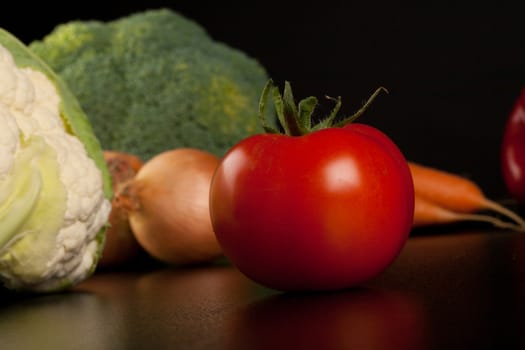 tomato on black with different vegetables in the background