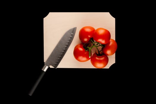 tomato with knife on wooden cutting board on black background