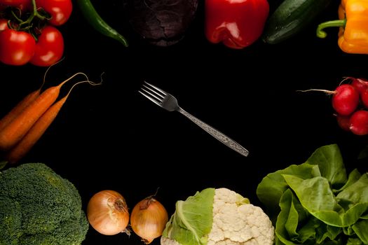 border made of different vegetables with fork in the middle on black background