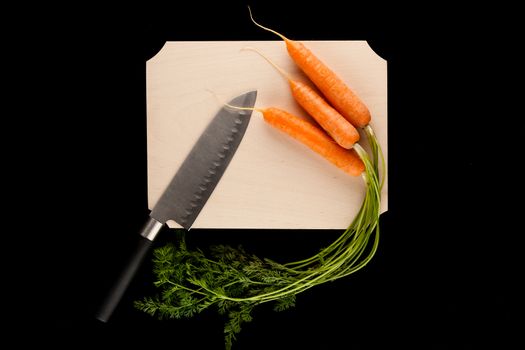 carrots with knife on wooden cutting board on black background