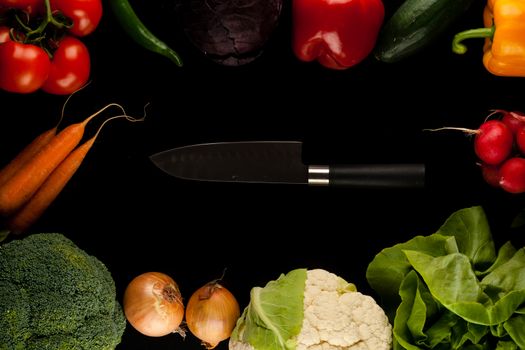 border made of different vegetables with knife in the middle on black background